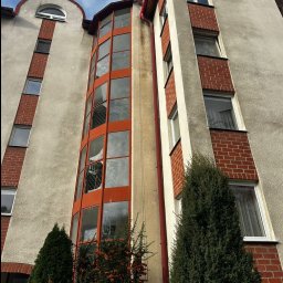 AlpinPeak - Wysoki budynek z przeszkloną, pomarańczową fasadą i ceglanymi elementami, widziany z dołu, z zielenią w tle. Widoczne odbicia w oknach.