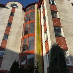 AlpinPeak - Wysoki budynek z widocznymi zabrudzeniami na elewacji, szczególnie wzdłuż rury spustowej. Ujęcie z dołu, podkreślające pionowość budynku i potrzebę interwencji.