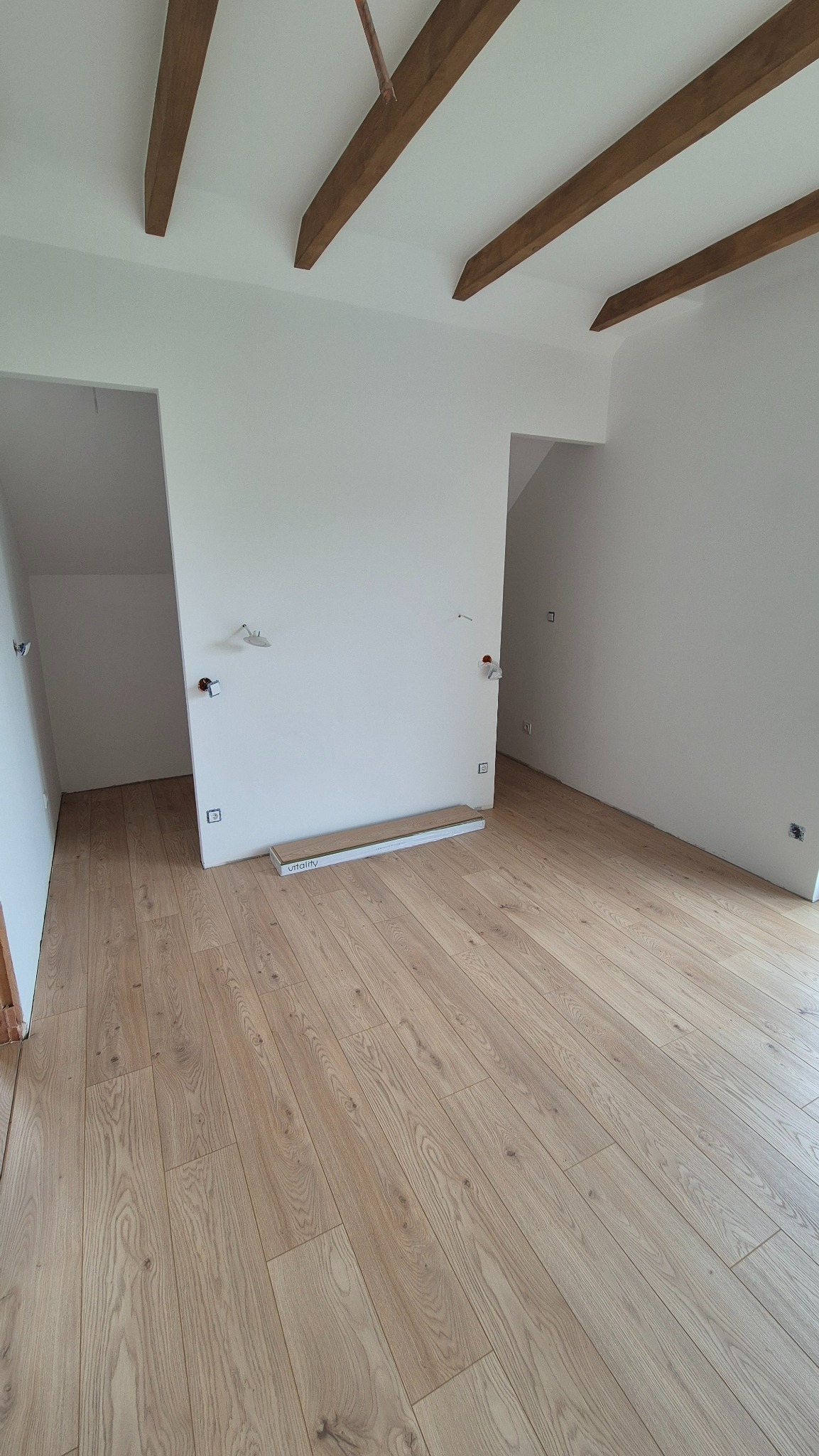 Jasne panele ułożone w pokoju ze ścianami pomalowanymi na biało i drewnianymi belkami na suficie w Sławkowie. Widoczne puszki elektryczne.