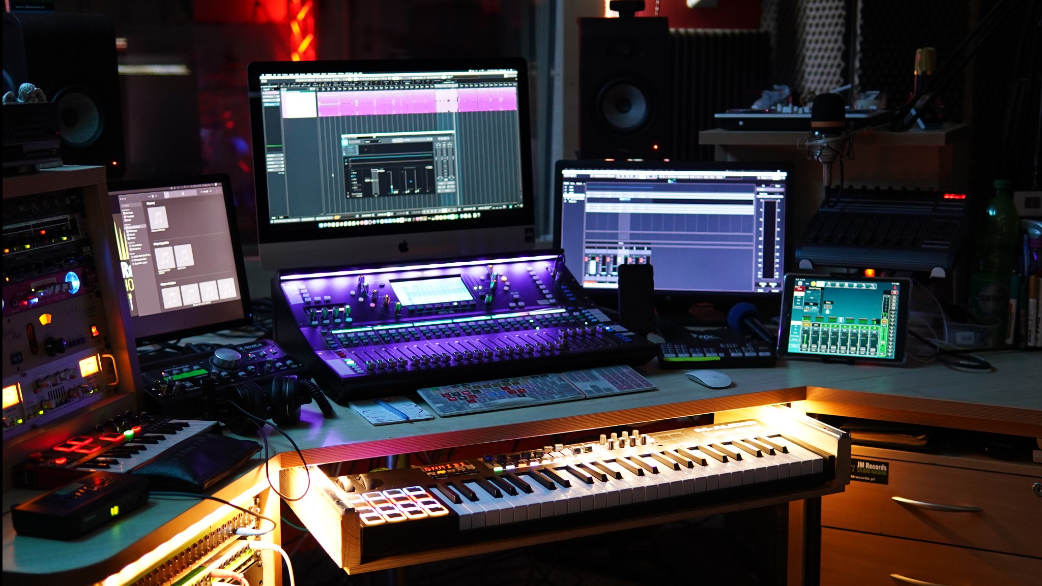 Profesjonalne studio nagrań z mikserem oświetlonym na fioletowo, klawiszami, monitorami z oprogramowaniem audio i sprzętem rackowym. Nowoczesna reżyserka.