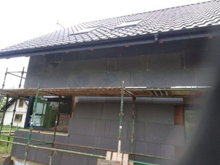 Ocieplanie elewacji budynku styropianem w Sianowie. Widoczne rusztowanie i fragment dachu z lukarną. Etap prac przed nałożeniem tynku.