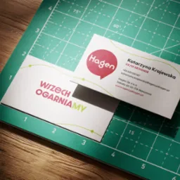 Dwie wizytówki firmy Hagen na zielonej macie do cięcia. Jedna z logo i hasłem 'Wszech Ogarniamy', druga z danymi kontaktowymi UX/UI Designera.