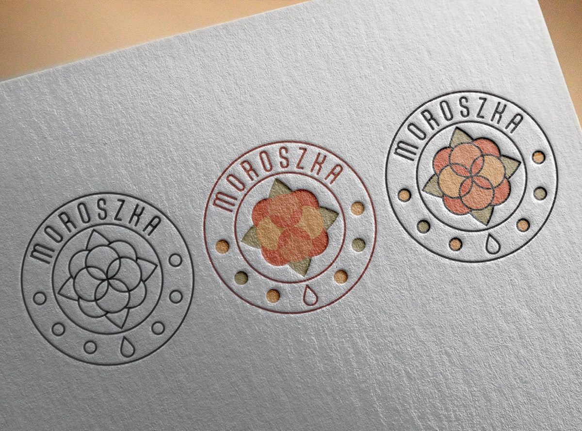 Trzy okrągłe, tłoczone logotypy 'Moroszka' na szarym papierze o subtelnej fakturze. Dwa logotypy z kolorowym wypełnieniem, jeden konturowy. Minimalistyczny design.