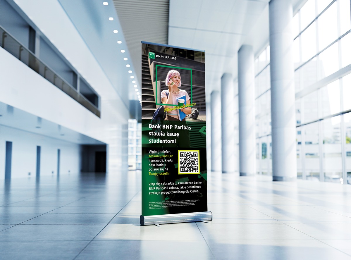 Roll-up Banku BNP Paribas z grafiką studentki i kodem QR na tle nowoczesnego wnętrza z kolumnami i dużymi oknami. Kampania reklamowa skierowana do studentów.