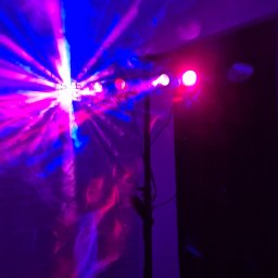 GOLDEN PARTY Łukasz Złoto - Efektowne oświetlenie dyskotekowe: reflektor LED na statywie, rzucający dynamiczne, kolorowe wiązki światła w odcieniach fioletu i niebieskiego na ścianę.