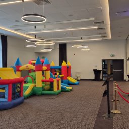 GOLDEN PARTY Łukasz Złoto - Kolorowe dmuchańce zamki w przestronnej sali z fotobudką Golden Party. Ustawione w rzędzie, gotowe do zabawy. Oświetlenie sufitowe, ciemne zasłony i wykładzina.