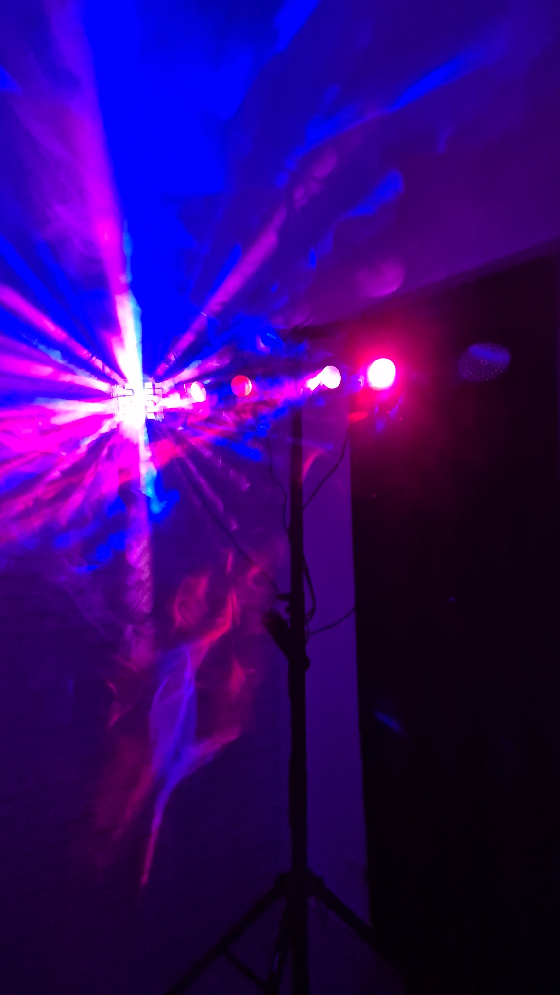 Efektowne oświetlenie dyskotekowe: reflektor LED na statywie, rzucający dynamiczne, kolorowe wiązki światła w odcieniach fioletu i niebieskiego na ścianę.