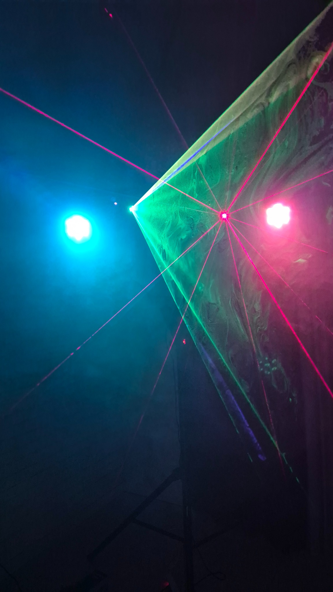 Dynamiczne oświetlenie laserowe: zielono-różowe wiązki przecinają ciemność, tworząc futurystyczny efekt wizualny na tle niebieskiego światła.