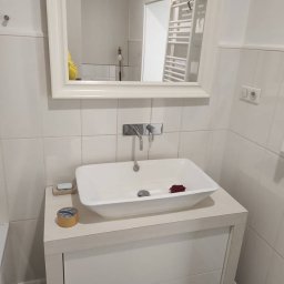 Patryk Siwicki - Biała umywalka nablatowa z lustrem w łazience wyłożonej białymi płytkami. Widoczne akcesoria: mydło, taśma klejąca. Nowoczesny wystrój, świeżo po remoncie.