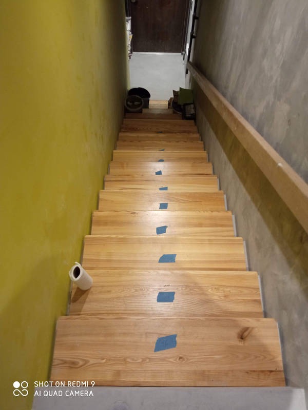 Schody drewniane zabezpieczone taśmą malarską przed malowaniem. Żółta ściana po lewej i surowy beton po prawej. Rolka papieru na pierwszym stopniu.