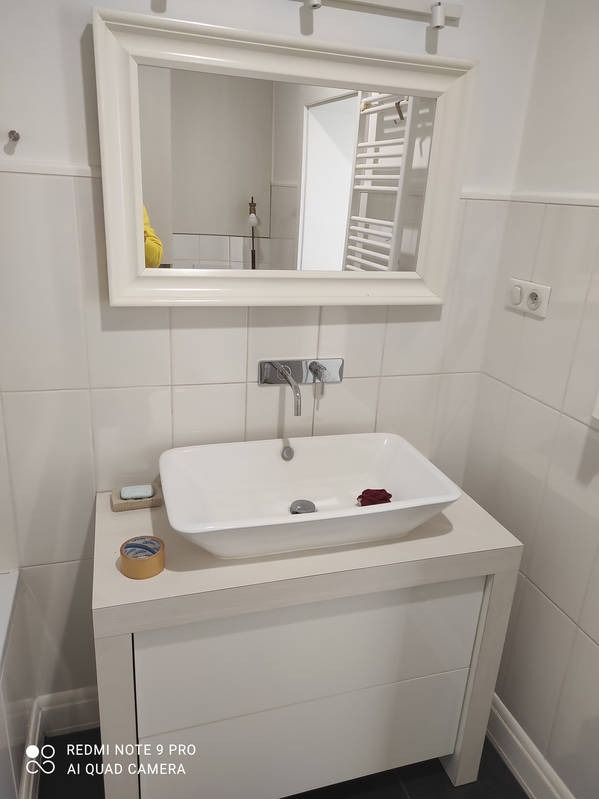 Biała umywalka nablatowa z lustrem w łazience wyłożonej białymi płytkami. Widoczne akcesoria: mydło, taśma klejąca. Nowoczesny wystrój, świeżo po remoncie.