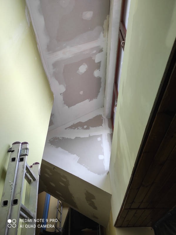 Wnętrze klatki schodowej w trakcie szpachlowania ścian i sufitu, widoczna drabina. Prace wykończeniowe w jasnej tonacji.