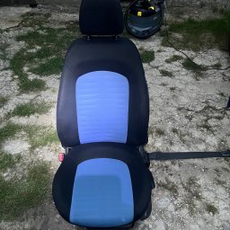 Bartłomiej Witczak - Wyjęty fotel samochodowy z niebieską tapicerką, obok odkurzacz piorący Karcher. Na zewnątrz, podłoże z kamieni i trawy. Widoczne ślady użytkowania.