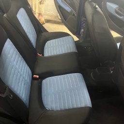 Bartłomiej Witczak - Wnętrze samochodu z czystymi, błękitnymi siedzeniami. Widoczne tylne fotele po detailingu, z wyraźną strukturą tapicerki. Otwarta boczna szyba auta.