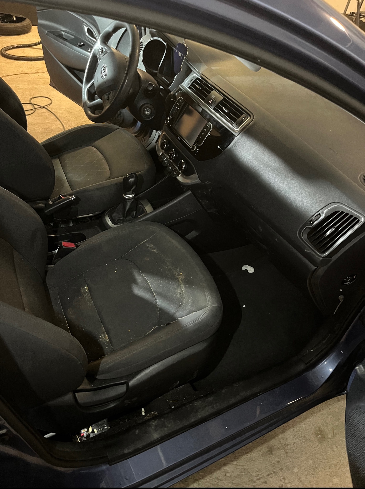 Wnętrze samochodu z wyraźnie zabrudzoną tapicerką foteli i dywaników, wymagające profesjonalnego czyszczenia. Widoczne plamy i okruchy.