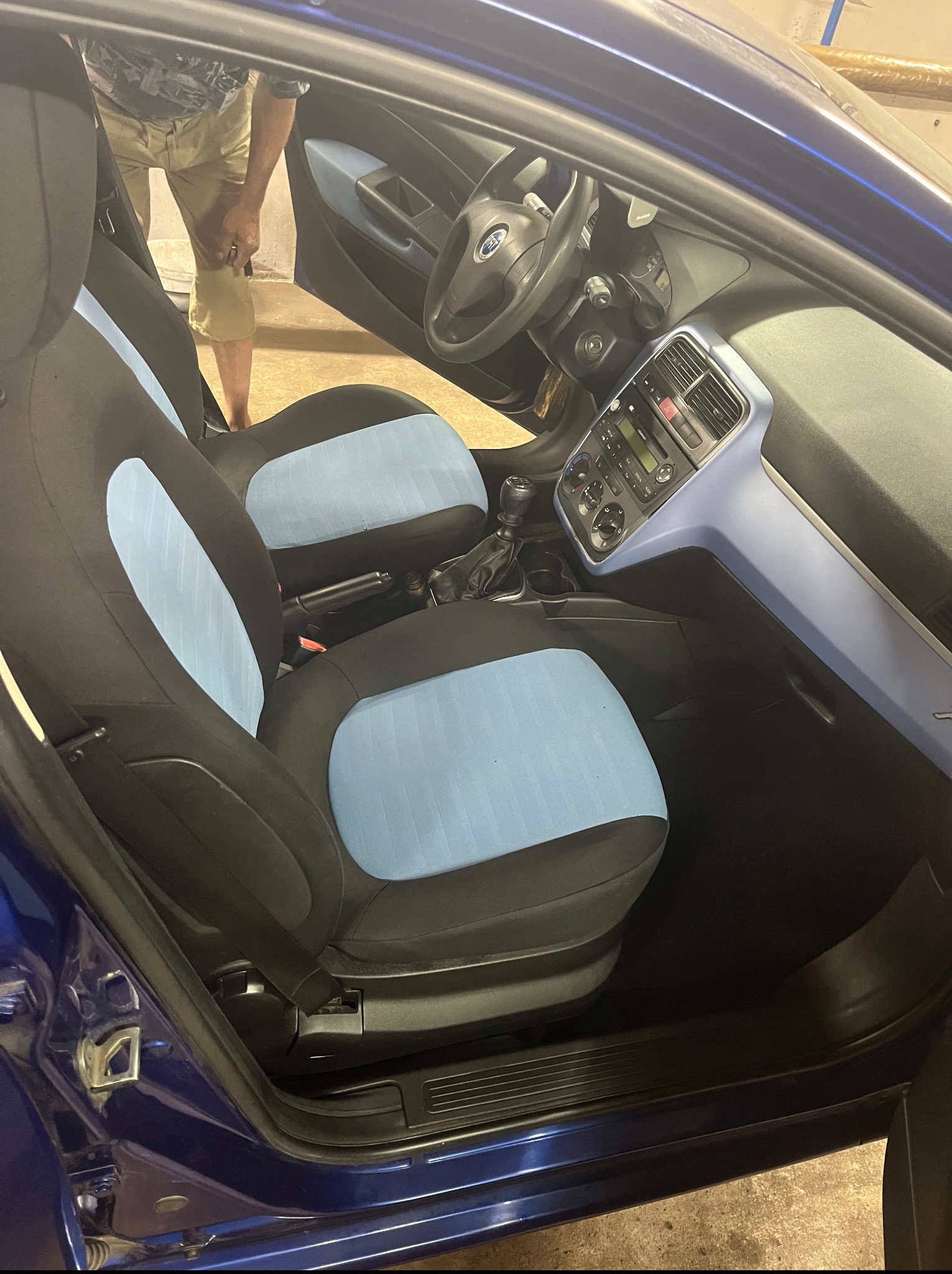 Wnętrze samochodu z czarno-błękitną tapicerką foteli, widoczne z zewnątrz przez otwarte drzwi. Deska rozdzielcza w kolorze błękitnym.