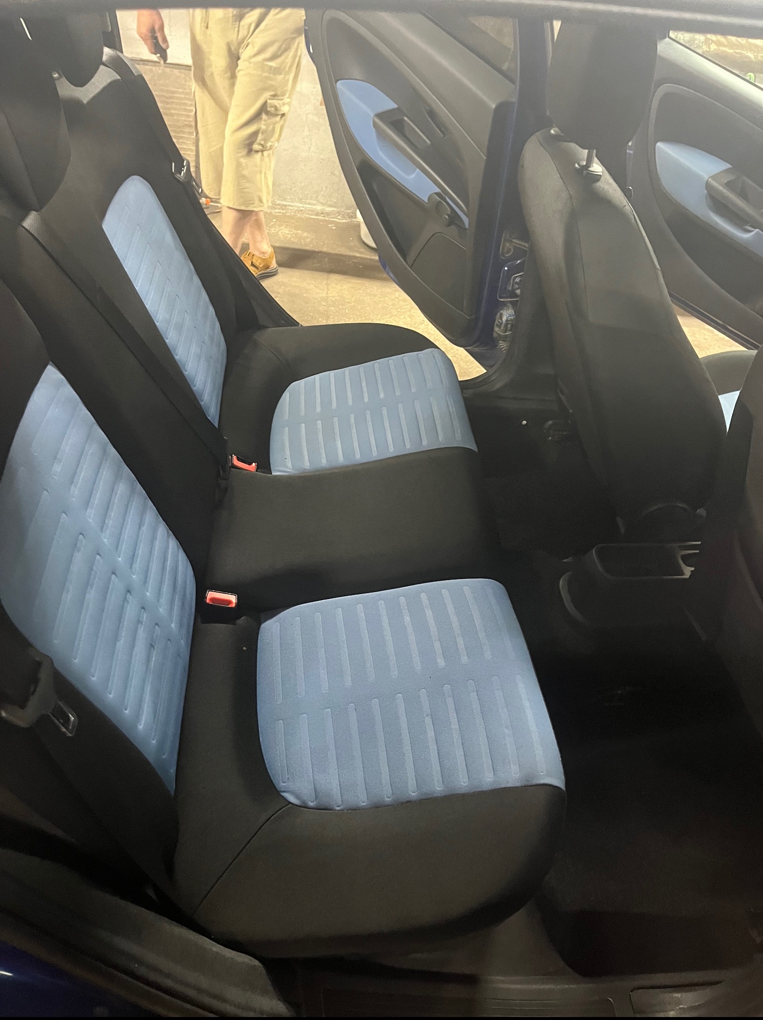 Wnętrze samochodu z czystymi, błękitnymi siedzeniami. Widoczne tylne fotele po detailingu, z wyraźną strukturą tapicerki. Otwarta boczna szyba auta.