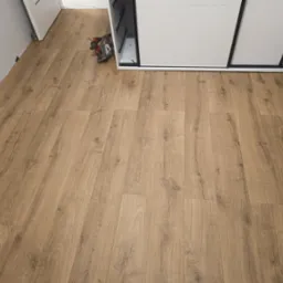 Ułożone panele podłogowe w odcieniach drewna, widoczne narzędzie do cięcia przy szafie przesuwnej. Nowa podłoga w jasnym wnętrzu.