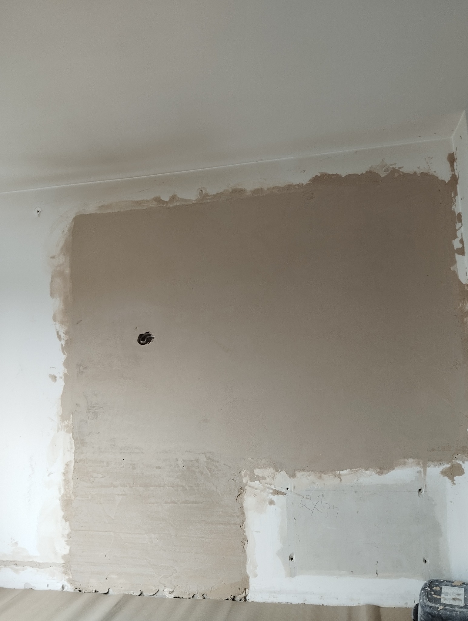 Fragment ściany w trakcie prac remontowych: częściowo nałożona gładź szpachlowa, widoczne ślady po instalacji elektrycznej, surowy stan wykończenia.