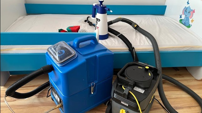 Niebieskie łóżko dziecięce z białym materacem, przygotowane do prania. Widoczne urządzenia do czyszczenia i akcesoria. Ujęcie z bliska, skupione na materacu.