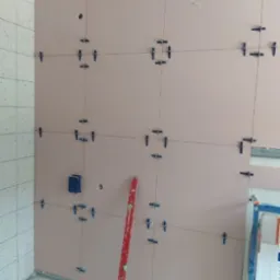 Montaż płyt karton-gips na ścianie z widocznymi łącznikami i poziomnicą. Instalacja elektryczna w puszce. Fragment ściany wykończony płytkami.