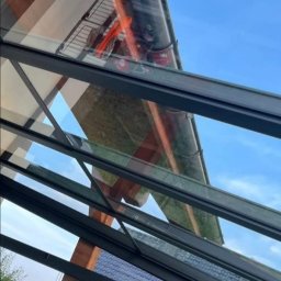 Dziemba Ci Umyje - Szklany dach z widocznym zanieczyszczeniem i odbiciem nieba, wymagający czyszczenia. Widoczne rynny i otoczenie domu.