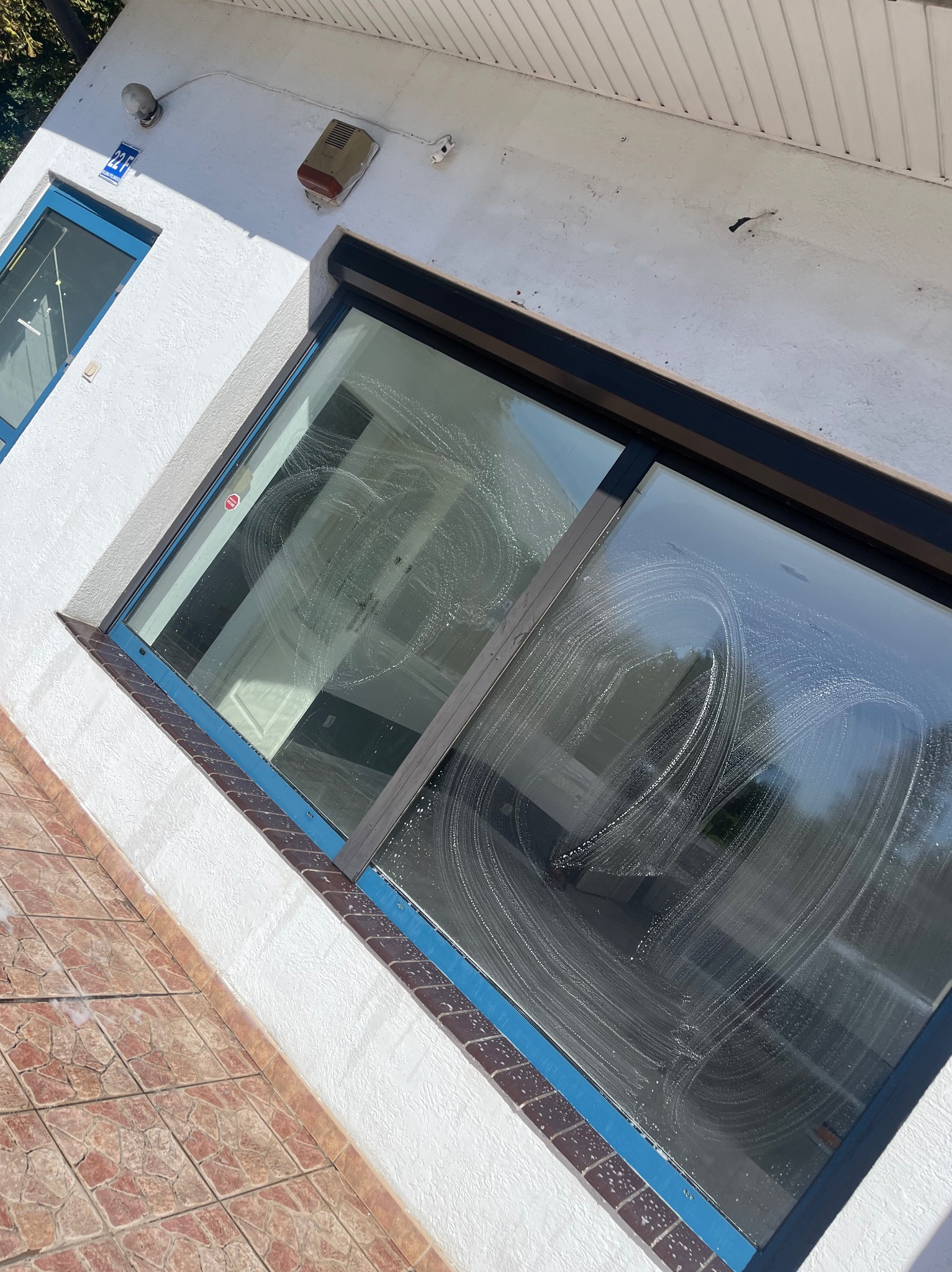 Okno z mydlinami w trakcie mycia, widoczne na białej fasadzie budynku z dekoracyjną cegłą. Ujęcie z dołu, widać fragment dachu i elewacji.