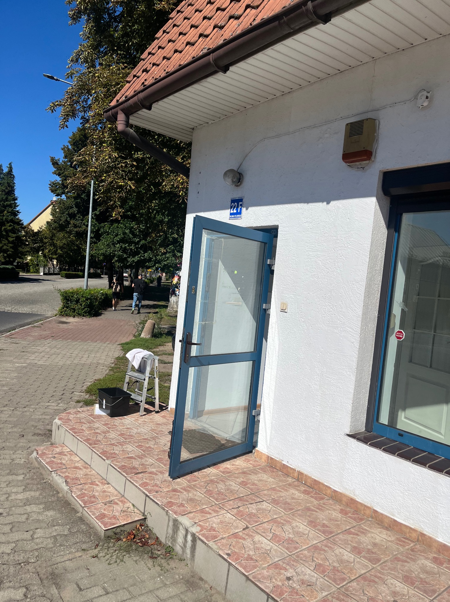 Otwarta szklana witryna budynku z numerem 22F, drabina z ręcznikiem i wiadro przy wejściu. Usługi czyszczenia witryn sklepowych.