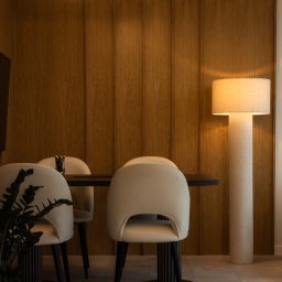 powab pracownia - Minimalistyczna jadalnia: drewniana ściana, lampa w kształcie liścia, beżowe krzesła i czarny stół. Stonowana kolorystyka i nowoczesny design.