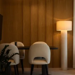 Minimalistyczna jadalnia: drewniana ściana, lampa w kształcie liścia, beżowe krzesła i czarny stół. Stonowana kolorystyka i nowoczesny design.