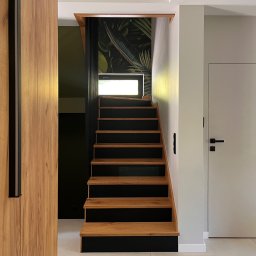 powab pracownia - Nowoczesne schody z drewnianymi stopniami i czarnymi podstopnicami, oświetlone światłem z okna, z widoczną tapetą w tropikalne liście w tle.