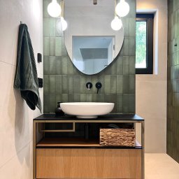 powab pracownia - Nowoczesna łazienka z umywalką nablatową, zielonymi płytkami na ścianie i drewnianą szafką. Minimalistyczne oświetlenie i lustro w owalnej ramie dodają elegancji.