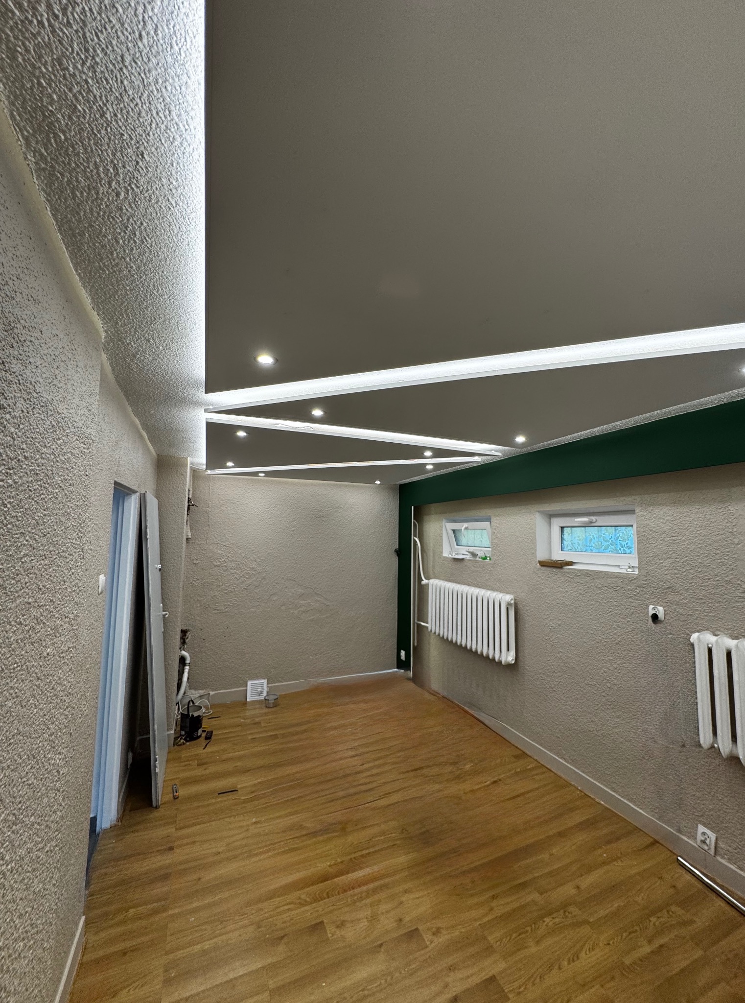 Nowoczesne oświetlenie LED w nowo wykończonym pokoju, z podwieszanym sufitem. Realizacja w Białymstoku. Widoczne grzejniki i drewniana podłoga.