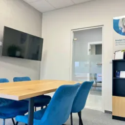 Nowoczesne biuro kredytowe w Krakowie: stół z krzesłami, plakat 'Kredyt hipoteczny', telewizor na ścianie. Minimalistyczny design, jasne wnętrze.