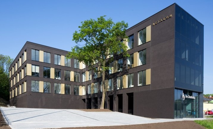 Nowoczesny budynek biurowy z ciemną elewacją i dużymi oknami, przed którym rośnie drzewo. Szklana fasada z nazwą firmy 'Ars Dentistica' w dolnej części.