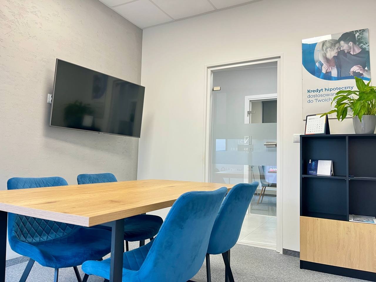Nowoczesne biuro kredytowe w Krakowie: stół z krzesłami, plakat 'Kredyt hipoteczny', telewizor na ścianie. Minimalistyczny design, jasne wnętrze.