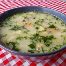 Kremowa zupa rybna z koperkiem w szarej misce na czerwono-białym obrusie w kratkę. Delikatne oświetlenie, ciepłe barwy, apetyczna prezentacja.