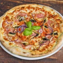 Apetyczna pizza z szynką, pieczarkami i czerwoną cebulą na cienkim cieście, udekorowana świeżą bazylią, serwowana na białym talerzu na drewnianym stole.