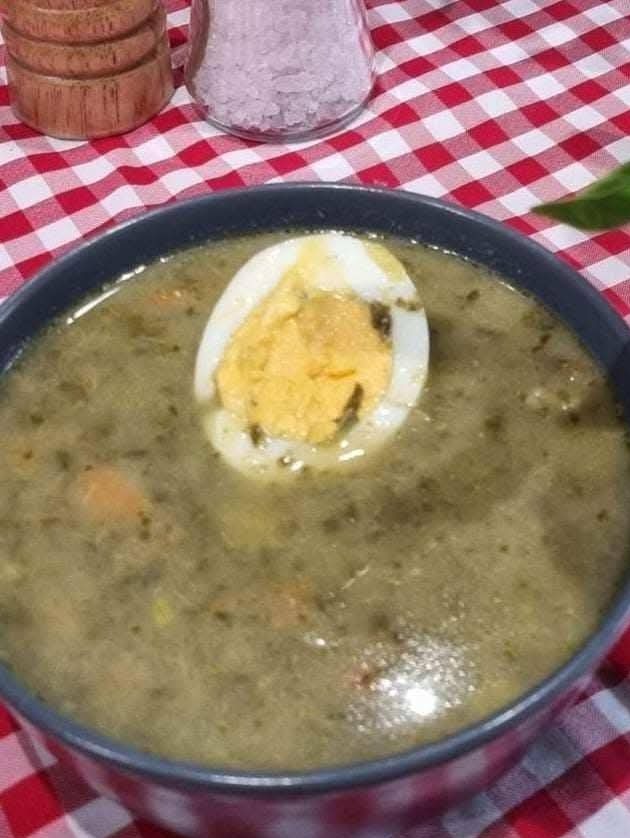 Talerz żurku z jajkiem na tle czerwono-białej kraty. W tle przyprawniki.