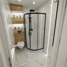 K.S bud - Wykończona łazienka z kabiną prysznicową w czarnej ramie, toaletą podwieszaną i marmurowymi płytkami, oświetlona ledami. Drewniane elementy dekoracyjne.