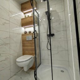 K.S bud - Nowoczesna łazienka z kabiną prysznicową typu walk-in, podwieszaną toaletą i drewnianymi półkami z oświetleniem LED, wykończona marmurowymi płytkami.