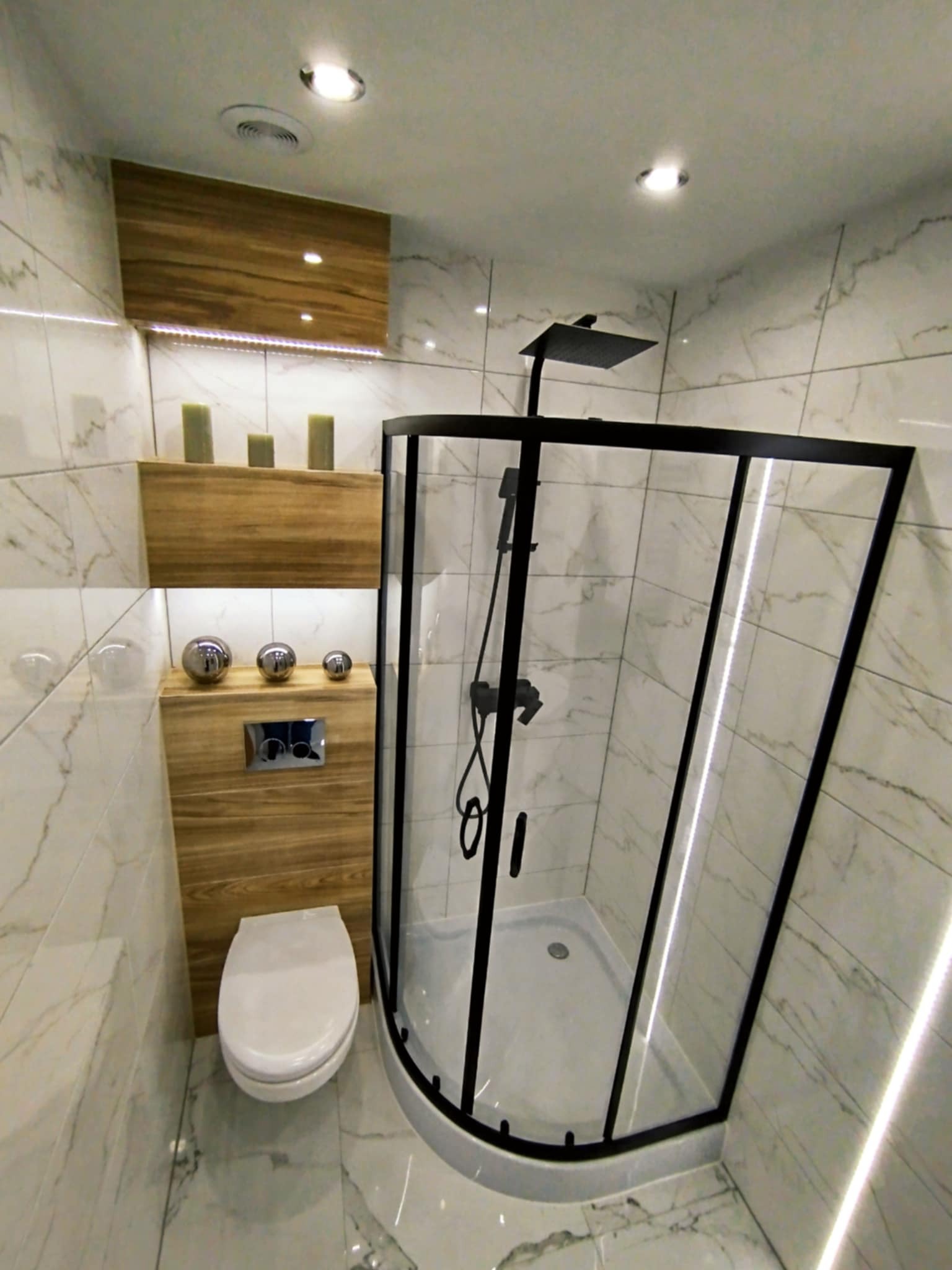 Nowoczesna łazienka z kabiną prysznicową typu walk-in z czarnymi profilami, marmurowe płytki, drewniane półki i podświetlenie LED. Minimalistyczny design.