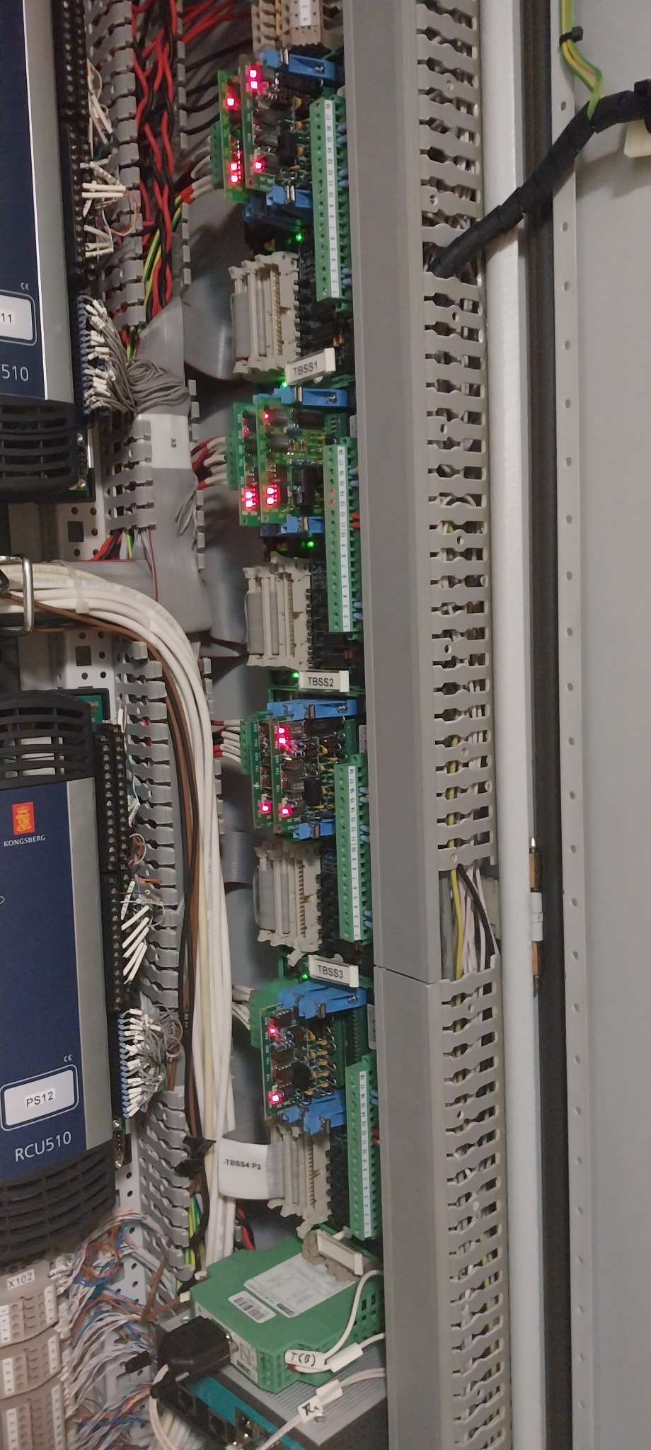 Wnętrze szafy sterowniczej z przewodami, modułami elektronicznymi i listwami DIN. Widoczne oznaczenia TBSS1, TBSS2, TBSS3, TBSS4. Czerwone i zielone diody LED.