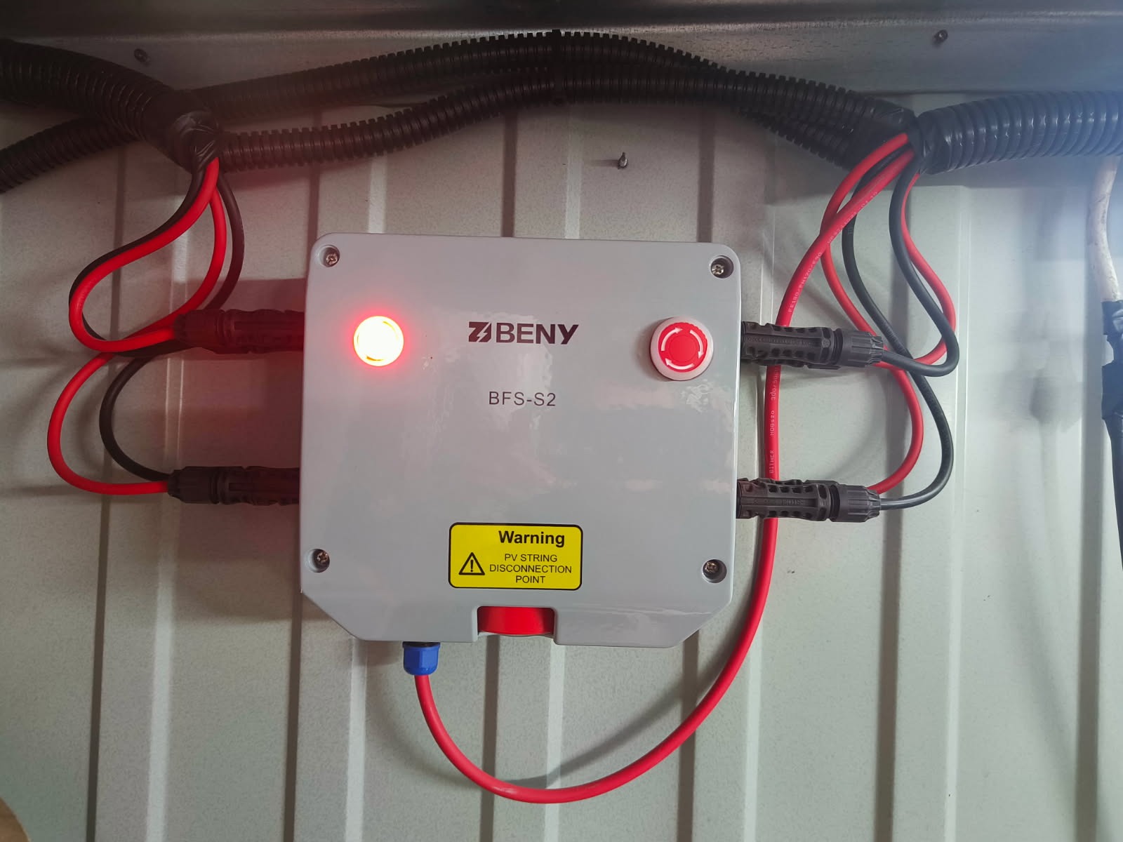 Szary rozłącznik prądu stałego BENY BFS-S2 z czerwonymi i czarnymi przewodami, ostrzeżeniem o odłączeniu PV, zamontowany na metalowej powierzchni.