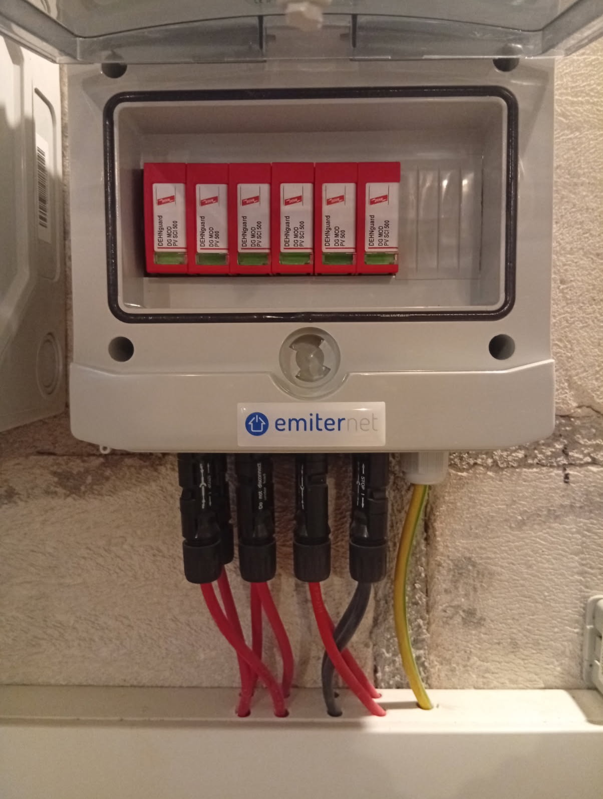Otwarta skrzynka z zabezpieczeniami DEHNguard DG MOD PV SCI 500, z widocznymi przewodami w kolorach czerwonym, szarym i żółto-zielonym, zamontowana na szarej ścianie.