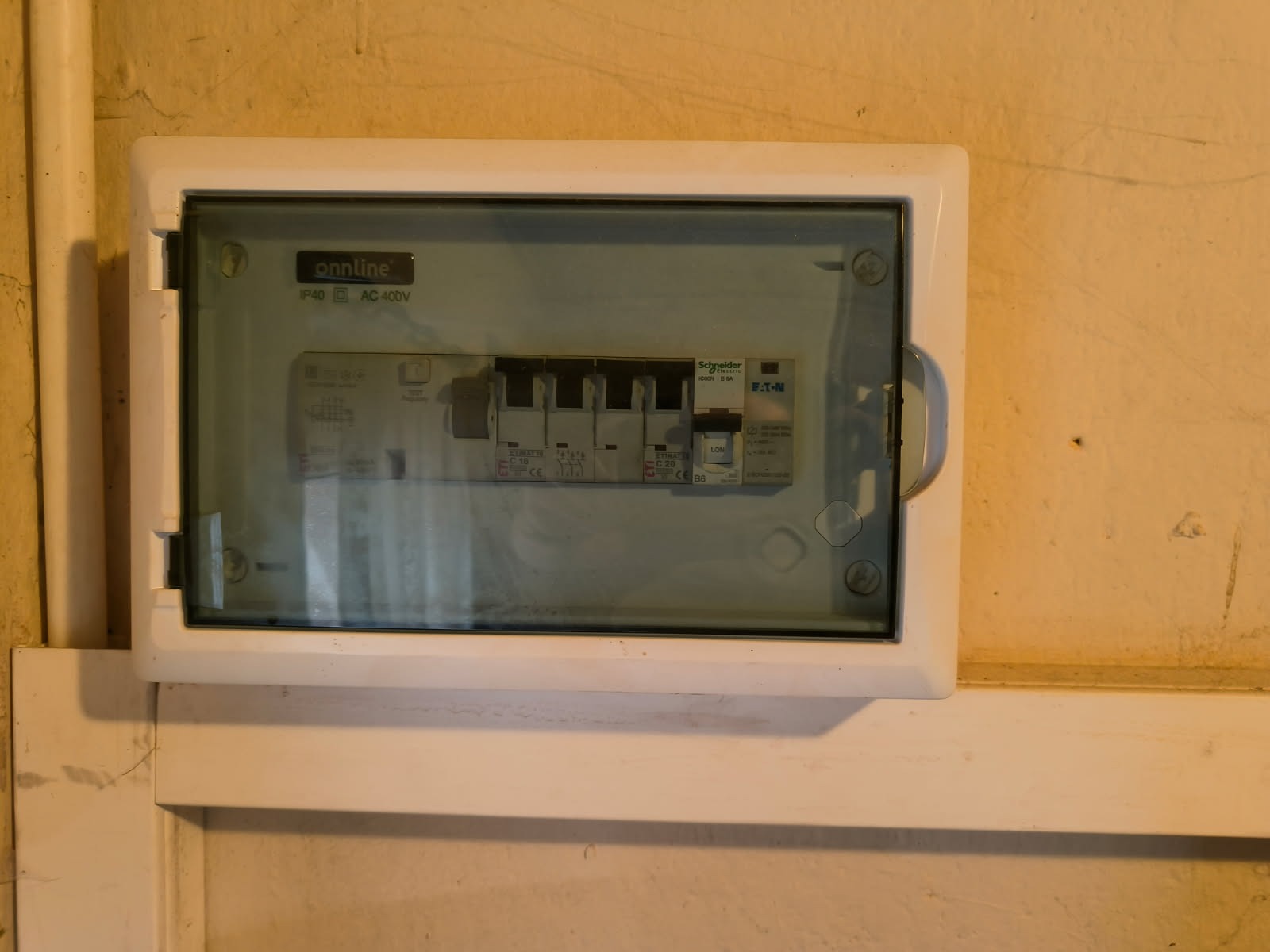 Zamknięta skrzynka elektryczna z bezpiecznikami marek Schneider i Eaton, zamontowana na ścianie. Widoczne oznaczenia IP40 i AC 400V.