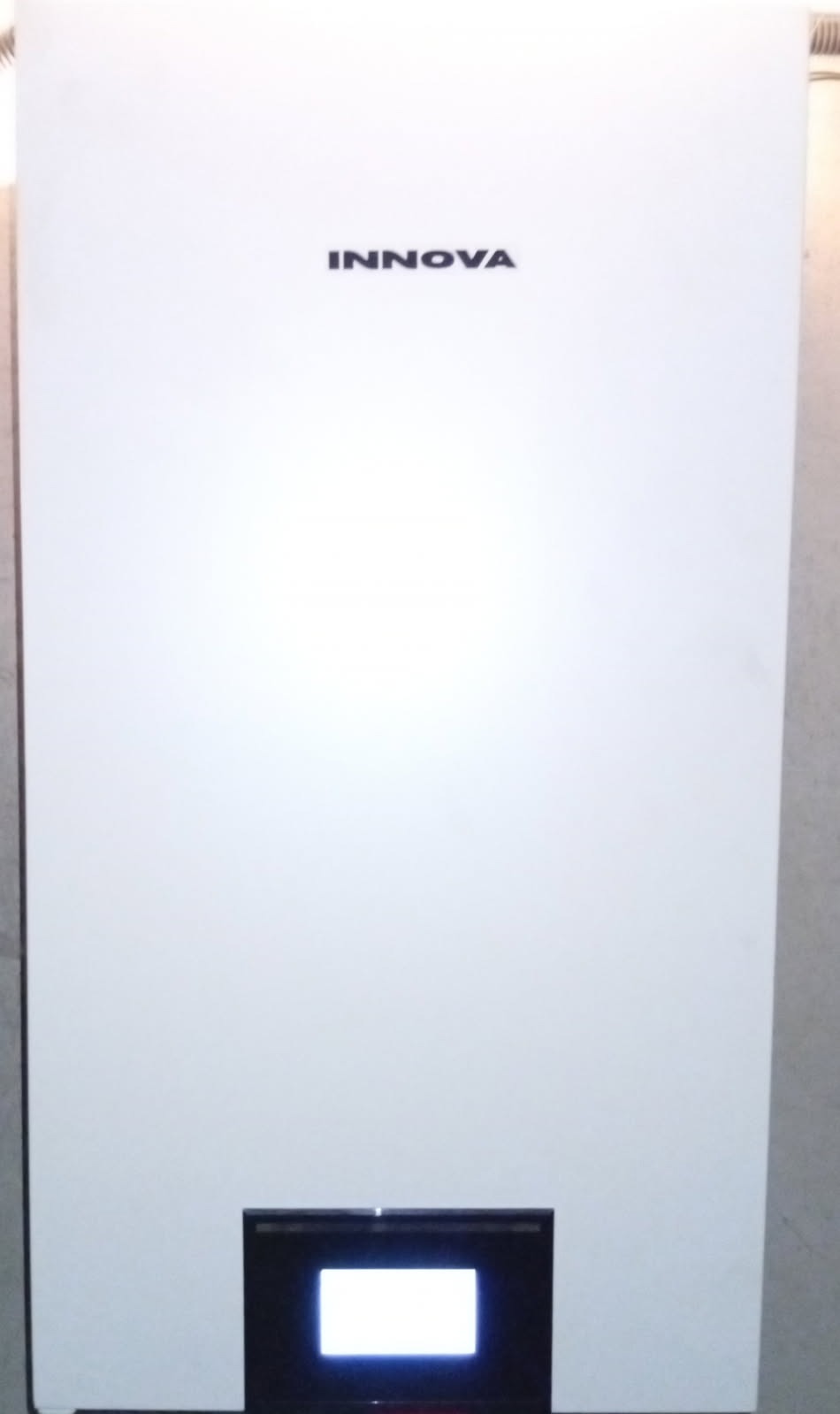 Biały, wiszący piec gazowy marki Innova z czarnym panelem sterowania i wyświetlaczem, zamontowany na ścianie. Widoczne delikatne oświetlenie boczne.