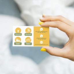 Klaudia Kozłowska Design - Dłoń z żółtym manicure trzyma wizytówkę firmy ogrodniczej z ikonami usług: nawadnianie, opieka, zakładanie trawników, renowacja ogrodów i danymi kontaktowymi.
