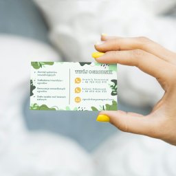 Klaudia Kozłowska Design - Dłoń prezentuje wizytówkę firmy ogrodniczej z zielonymi elementami graficznymi i danymi kontaktowymi, w tym adres e-mail i numery telefonów.