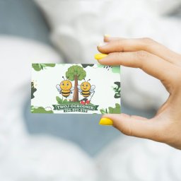 Klaudia Kozłowska Design - Dłoń z żółtym manicure trzyma wizytówkę z ilustracją dwóch pszczół, drzewa i kosiarki. Napis: Twój Ogrodnik, numer telefonu. Pastelowe tło.